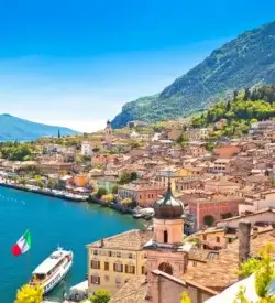 Udsigt over Gardasøen og byen Limone sul Garda med citrontræer, søpromenade og bjerglandskab i baggrunden, Limone sul Garda Italien. Togrejser Europa
