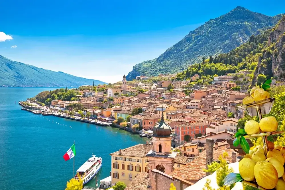 Udsigt over Gardasøen og byen Limone sul Garda med citrontræer, søpromenade og bjerglandskab i baggrunden, Limone sul Garda Italien. Togrejser Europa